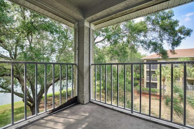 A balcony with a metal railing overlooks a grassy area, trees, and a neighboring apartment building — 2690 CORAL LANDINGS BOULEVARD UNIT 438, PALM HARBOR, FL
