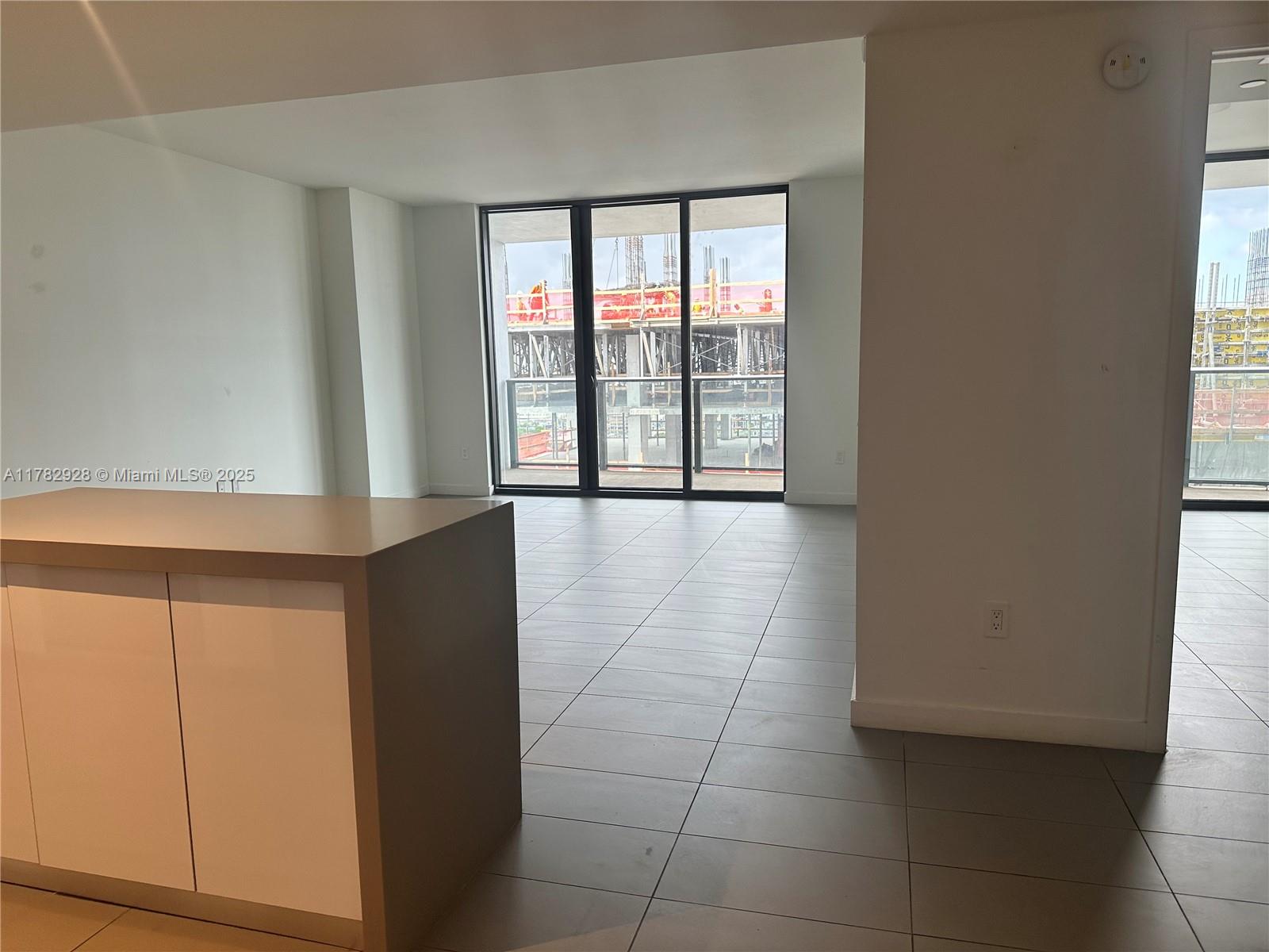 An unfurnished room with tile flooring, a kitchen island, and large windows overlooking a construction site — 1600 NE 1st Ave # 2017, Miami FL 33132, MIAMI, FL