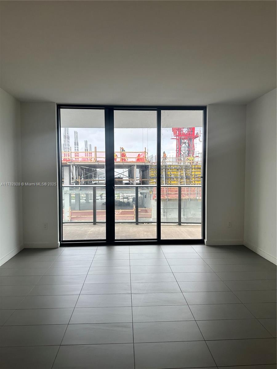 An empty room with gray tile flooring features a large sliding glass door overlooking construction — 1600 NE 1st Ave # 2017, Miami FL 33132, MIAMI, FL