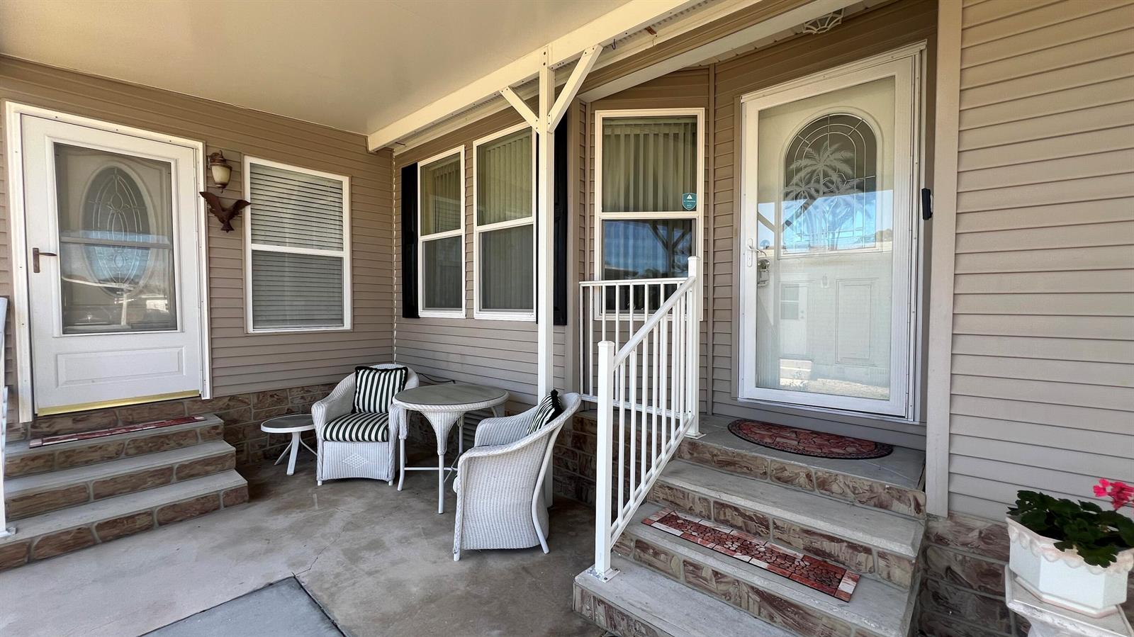 A covered patio features two white wicker chairs, a small table, and two entry doors — 621 Puffin Drive, Barefoot Bay FL 32976, BAREFOOT BAY, FL