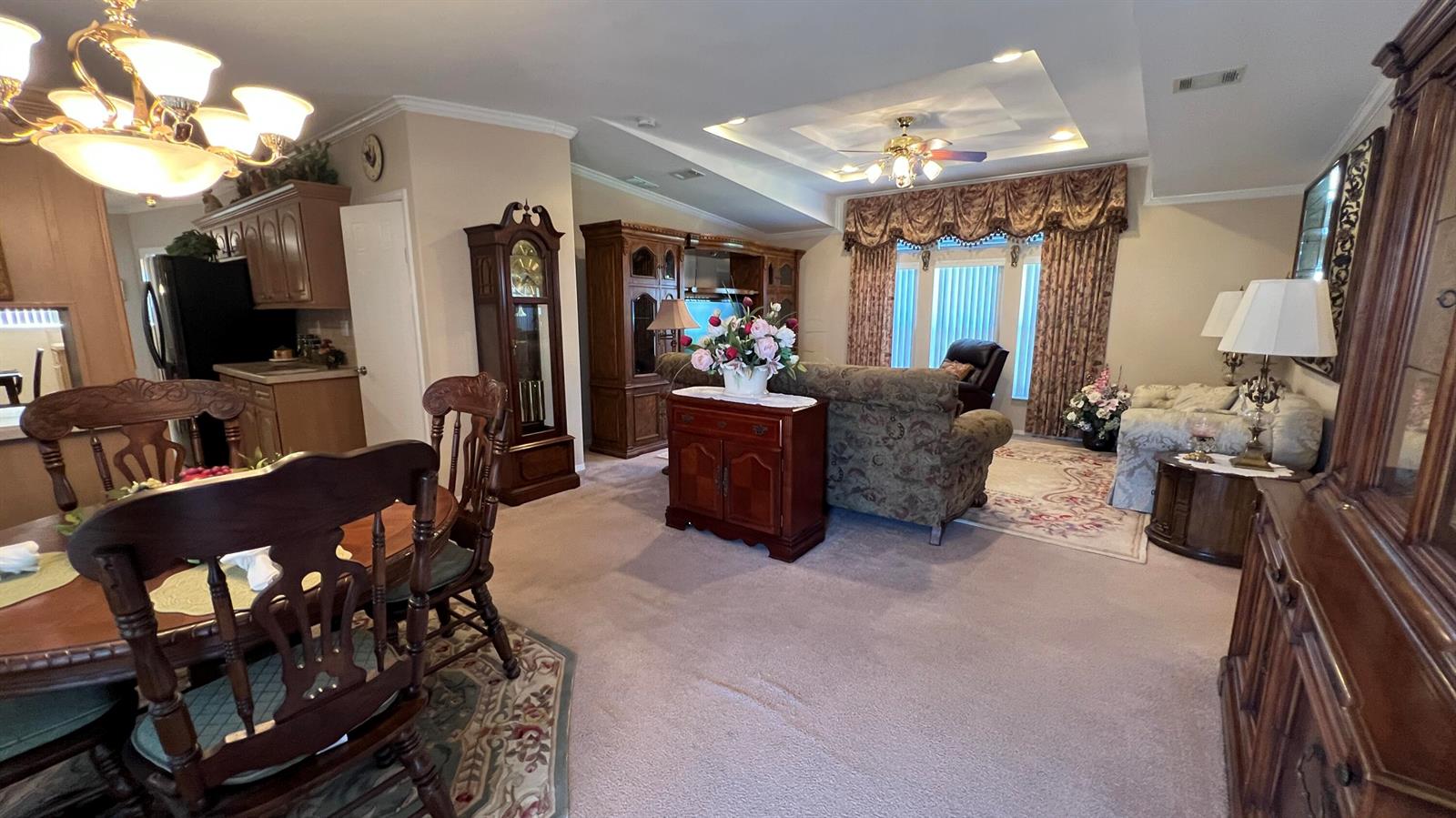 A living room and dining area feature traditional wooden furniture, carpeted floors, and patterned curtains — 621 Puffin Drive, Barefoot Bay FL 32976, BAREFOOT BAY, FL