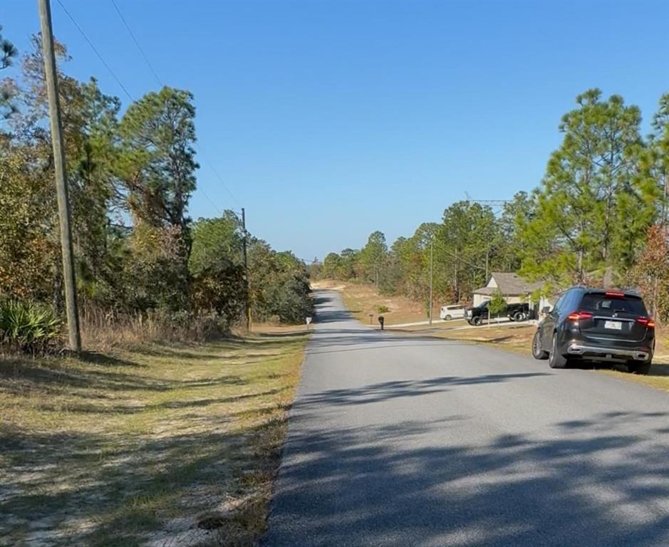 A paved road stretches into the distance, flanked by trees and a parked black SUV — 6783 N PAVILION LOOP, CITRUS SPRINGS, FL