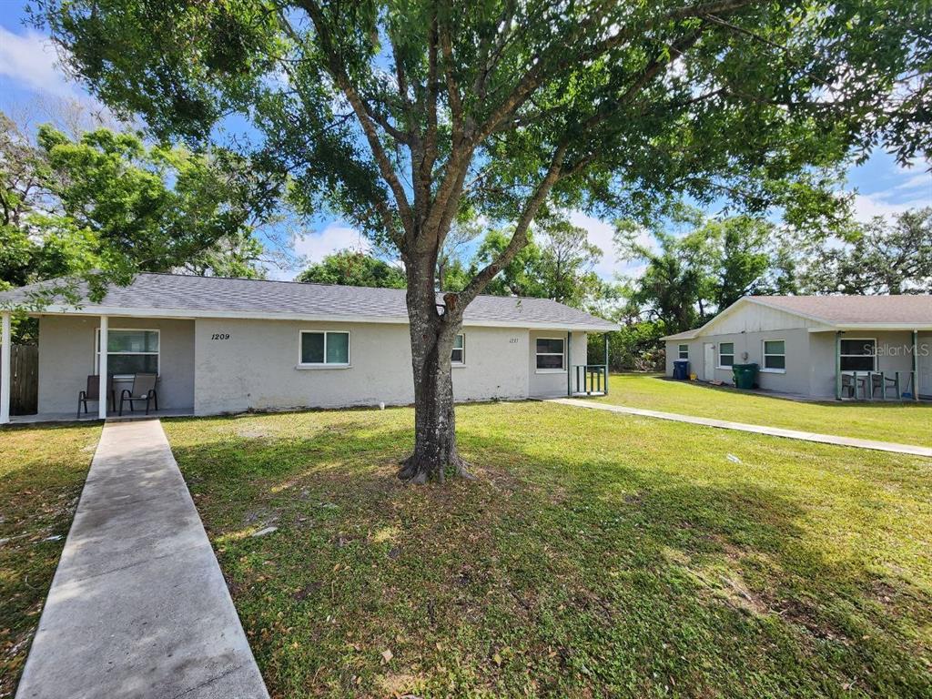Two single-story residential buildings with gray siding stand on a grassy lot with trees — 1209 62ND AVENUE E, BRADENTON, FL