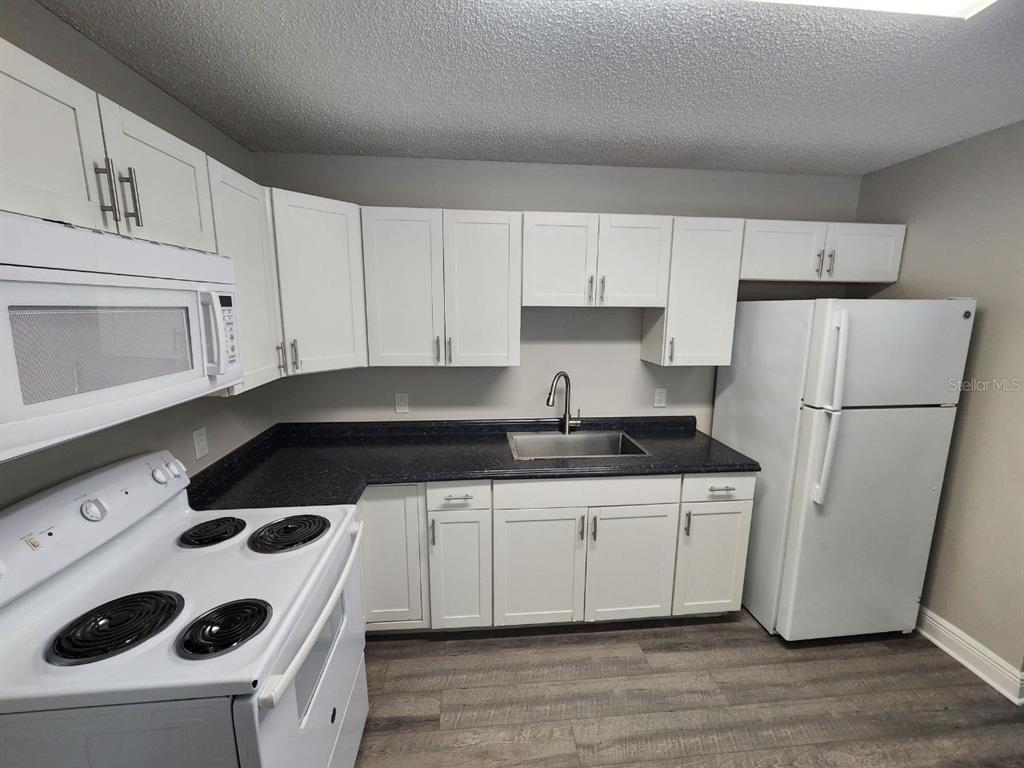 A kitchen features white cabinets, black countertops, a white stove, and a white refrigerator — 1209 62ND AVENUE E, BRADENTON, FL