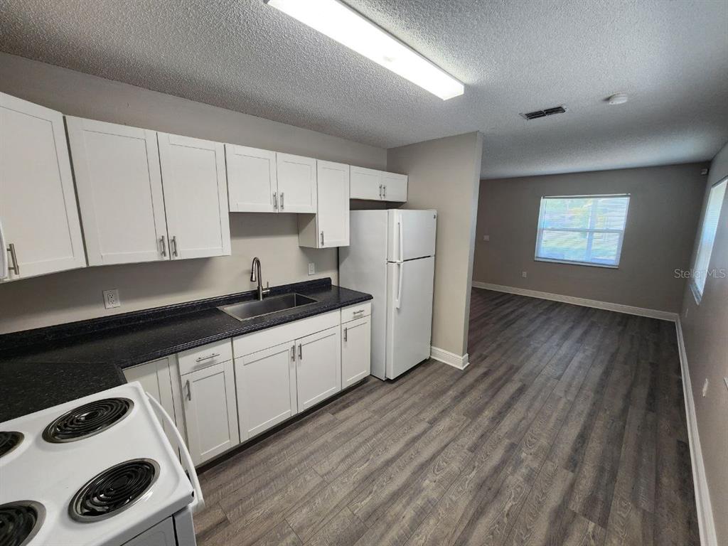 A kitchen with white cabinets, black countertops, and a white refrigerator opens to a living area — 1209 62ND AVENUE E, BRADENTON, FL