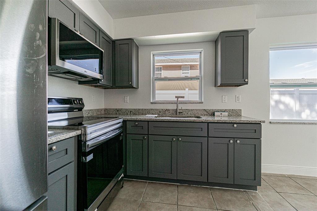 A kitchen features dark gray cabinets, granite countertops, stainless steel appliances, and tile flooring — 558 CLEARWATER LARGO ROAD N UNIT 1, LARGO, FL