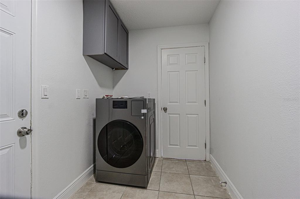 A laundry room features a gray front-load washer, a wall-mounted cabinet, and tile flooring — 558 CLEARWATER LARGO ROAD N UNIT 1, LARGO, FL
