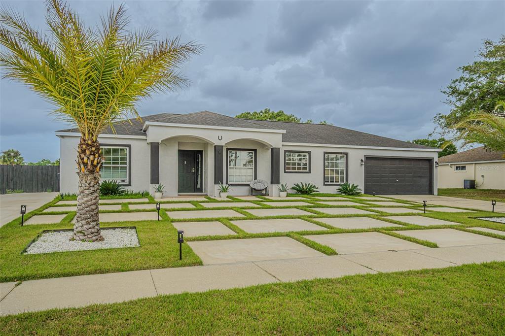 A single-story house with a gray exterior, dark garage door, and a grid-patterned concrete driveway — 12121 COLONIAL ESTATES LANE, RIVERVIEW, FL