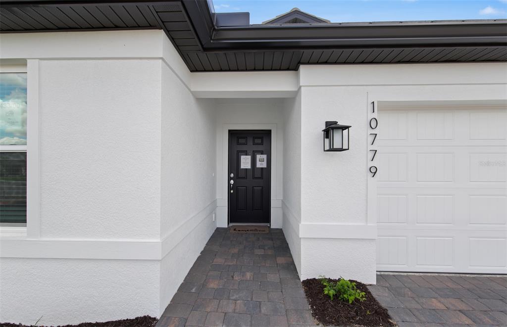 A white stucco house exterior features a black front door and a white garage door — 10779 SUN DROP STREET, VENICE, FL