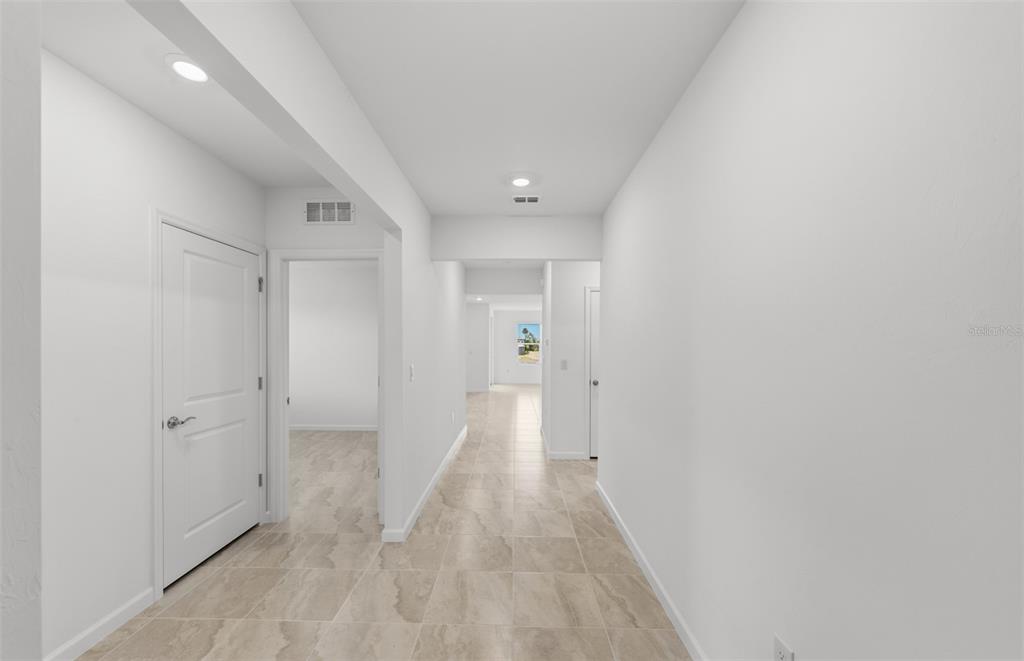 A bright hallway with light-colored tile flooring leads to a distant room with a window — 10779 SUN DROP STREET, VENICE, FL