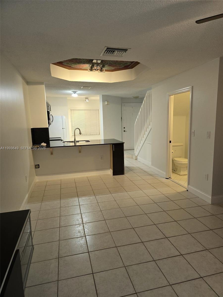 A kitchen with a breakfast bar and tile flooring opens to a staircase and bathroom — 14272 SW 121st Pl # 9, Miami FL 33186, MIAMI, FL