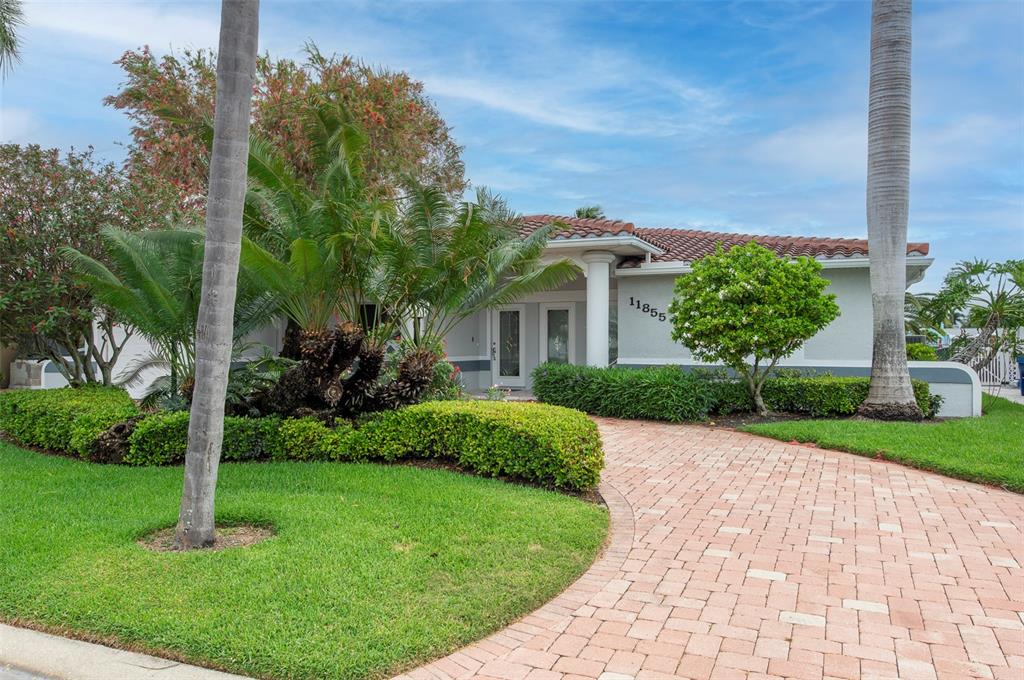 A single-story house with a tiled roof, palm trees, and a brick paver driveway — 11855 4TH STREET E, TREASURE ISLAND, FL