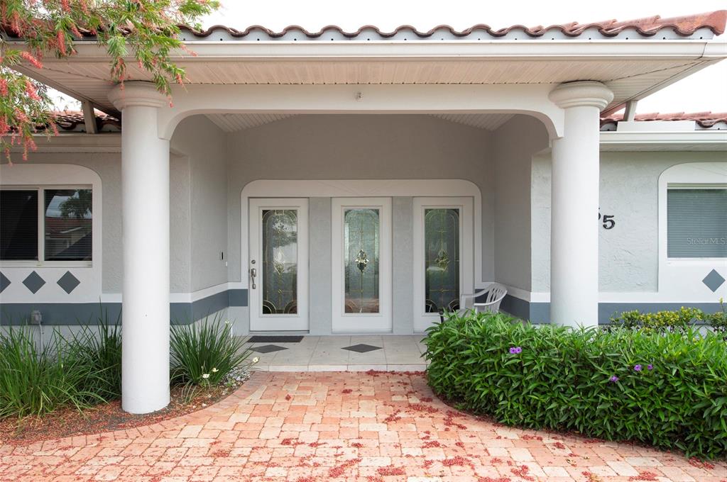 A covered entryway features a brick paver walkway, two white columns, and a triple-door entrance — 11855 4TH STREET E, TREASURE ISLAND, FL