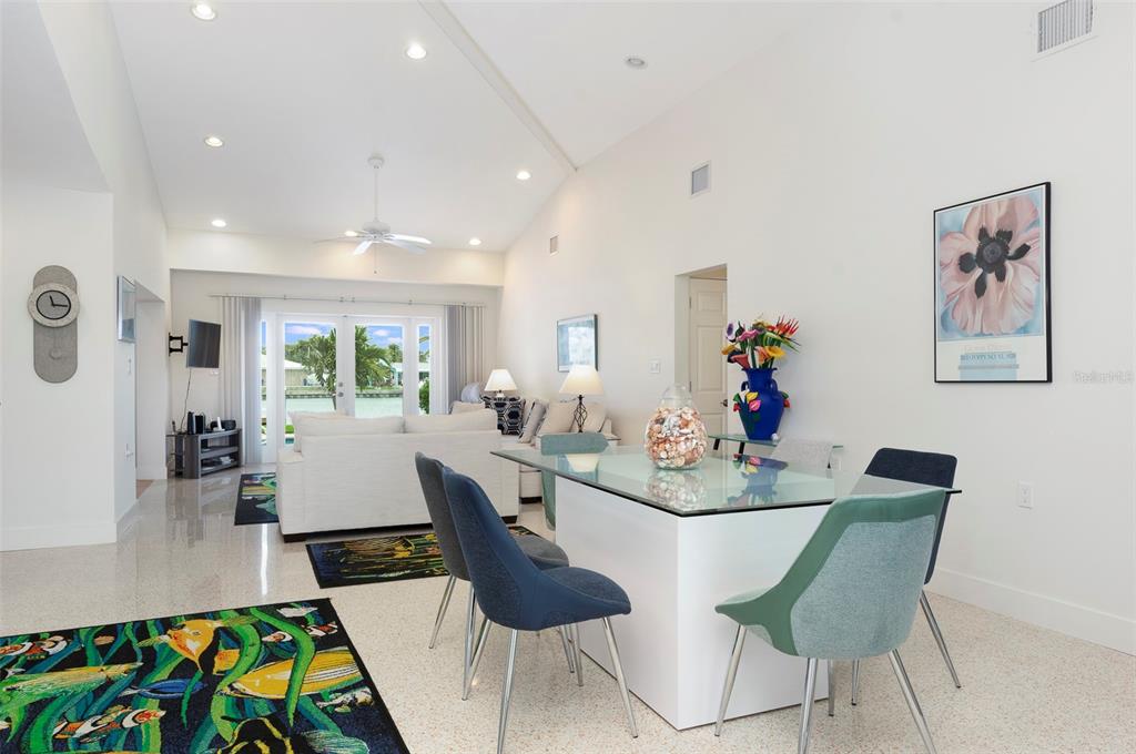 A bright, open-concept living and dining area features a glass-top table and water views — 11855 4TH STREET E, TREASURE ISLAND, FL