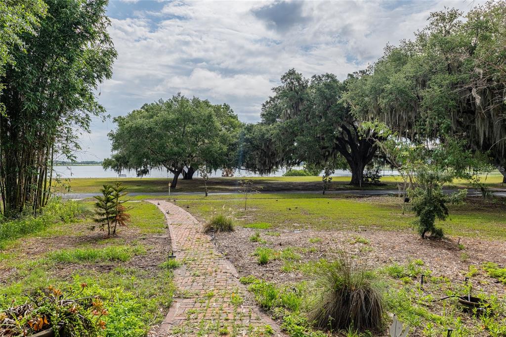 A brick path leads through a grassy yard toward large oak trees and a lake — 116 S LAKESHORE BOULEVARD, LAKE WALES, FL