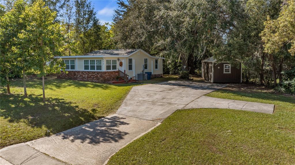 A light-colored house with a brick base, a concrete driveway, and a detached storage shed — 172 S VIRGINIA AVENUE, CENTER HILL, FL