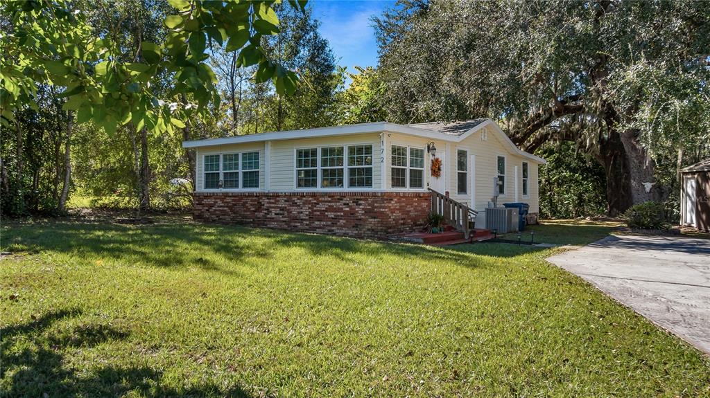 A single-story house with yellow siding and a brick base sits on a grassy lot — 172 S VIRGINIA AVENUE, CENTER HILL, FL