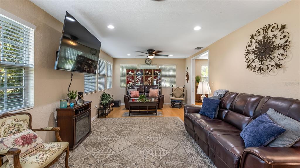 A living room features a brown leather sofa, a patterned rug, and a wall-mounted television — 172 S VIRGINIA AVENUE, CENTER HILL, FL