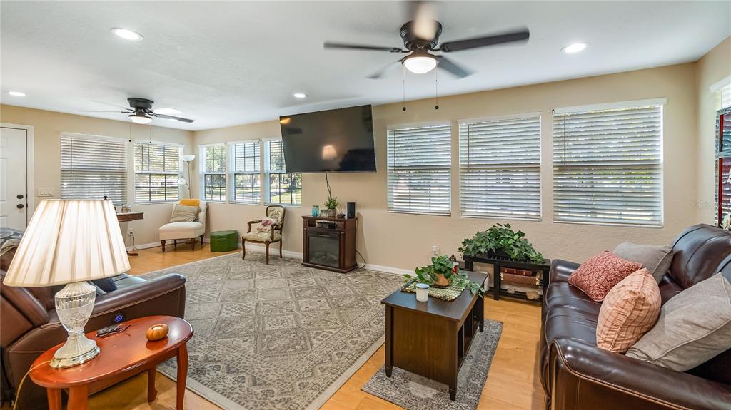 A living room with a large television, leather furniture, ceiling fans, and multiple windows — 172 S VIRGINIA AVENUE, CENTER HILL, FL
