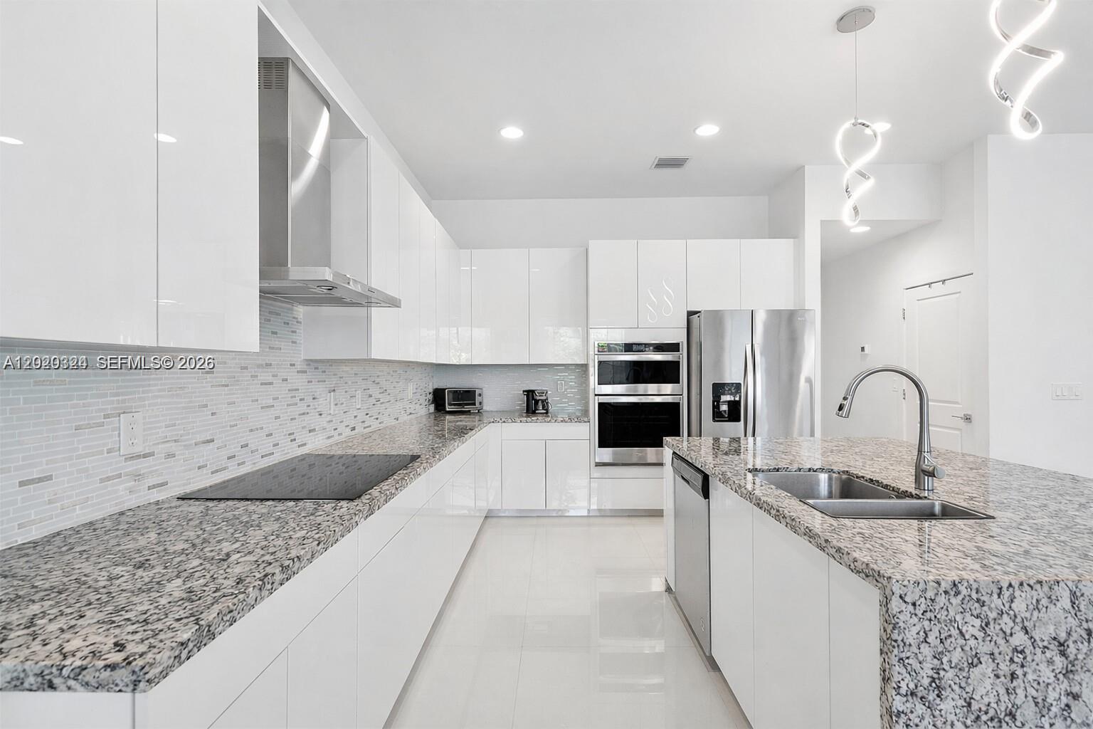 A modern kitchen features white glossy cabinets, granite countertops, stainless steel appliances, and tile flooring — 4406 SW 178th Ave, Miramar FL 33029, MIRAMAR, FL