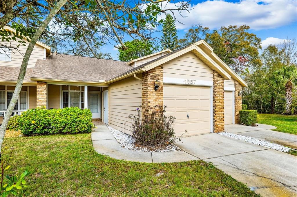 A tan-sided house with a brick-accented garage and a front walkway surrounded by landscaping — 4557 GLEN HOLLOW, NEW PORT RICHEY, FL