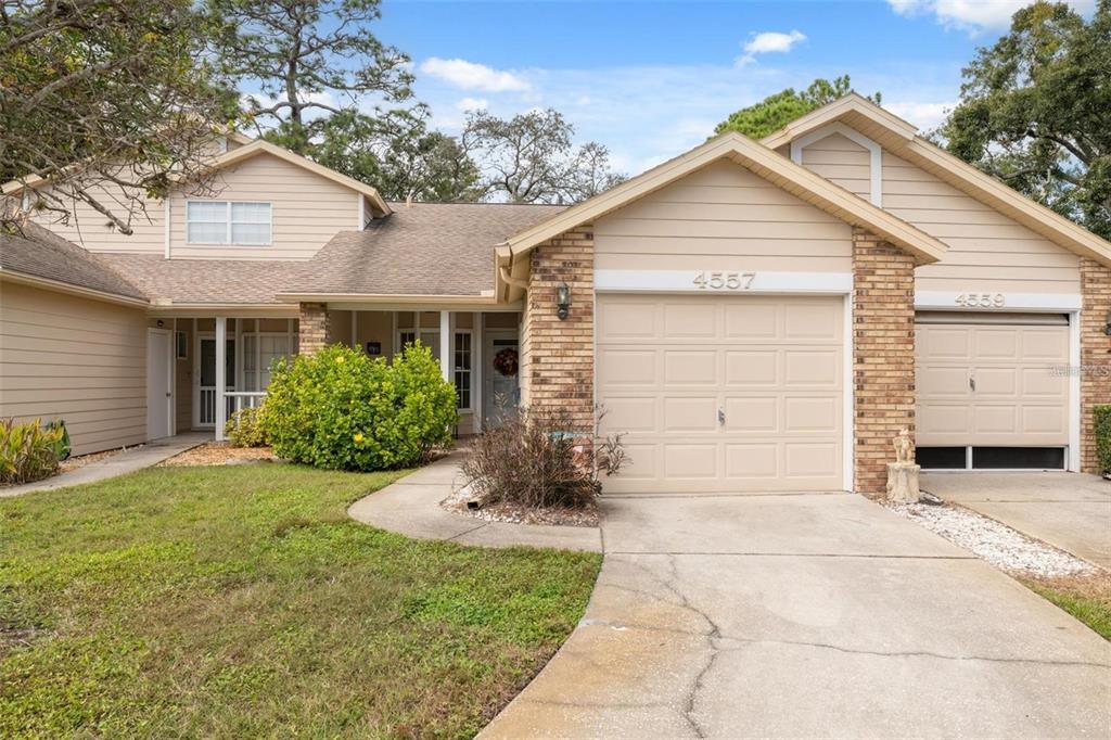 A tan-sided house with a brick facade, two garage doors, and a landscaped front yard — 4557 GLEN HOLLOW, NEW PORT RICHEY, FL