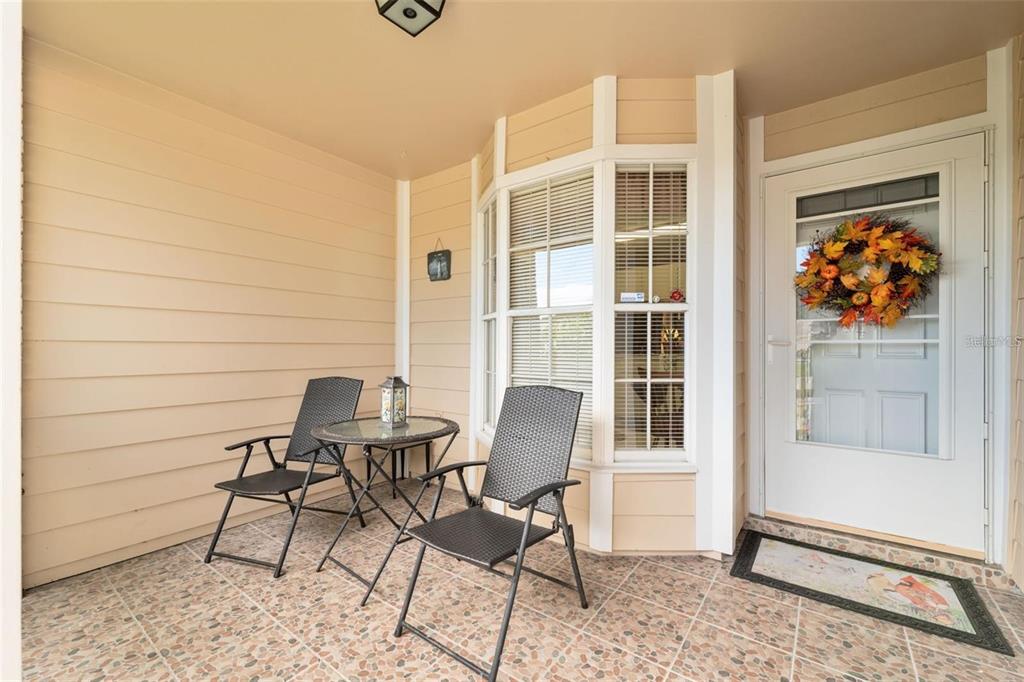 A covered front porch features a tiled floor, two chairs, a small table, and a door — 4557 GLEN HOLLOW, NEW PORT RICHEY, FL