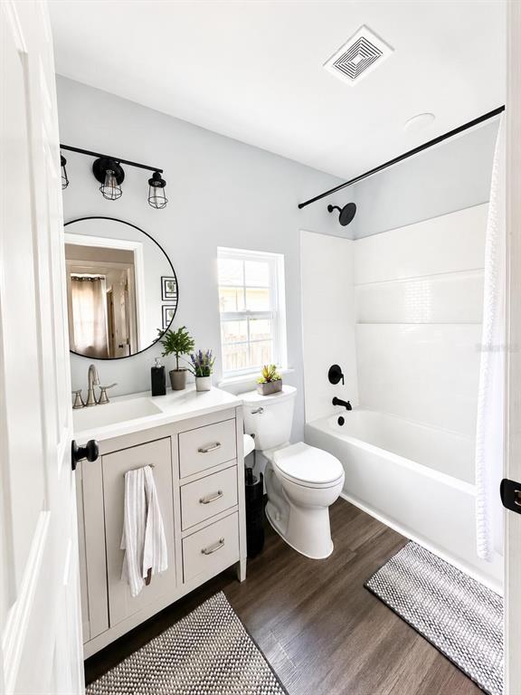 A bathroom features a light gray vanity, a round mirror, and a white tub-shower combo — 6306 HILL ROAD, ORLANDO, FL