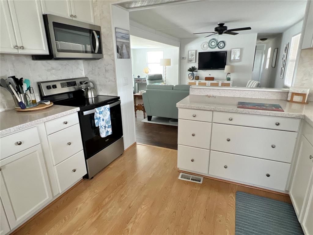 A kitchen with white cabinets and stainless steel appliances opens into a living room area — 614 MOUNT KEY AVENUE NE UNIT 631, ST PETERSBURG, FL