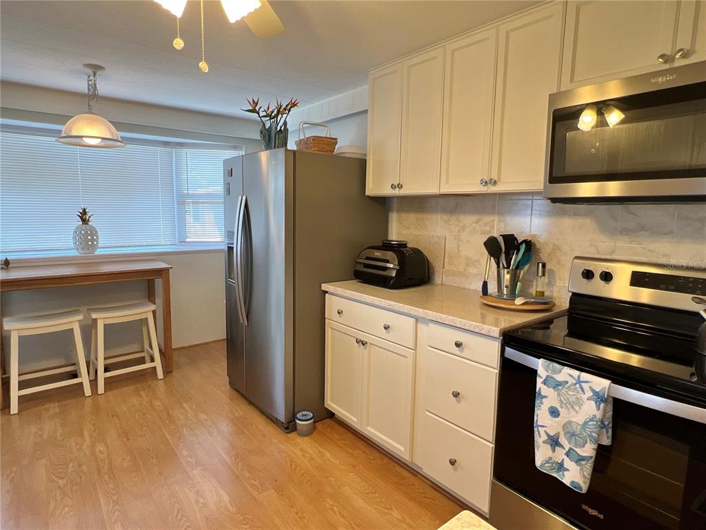 A kitchen features white cabinets, stainless steel appliances, a breakfast bar, and wood-look flooring — 614 MOUNT KEY AVENUE NE UNIT 631, ST PETERSBURG, FL