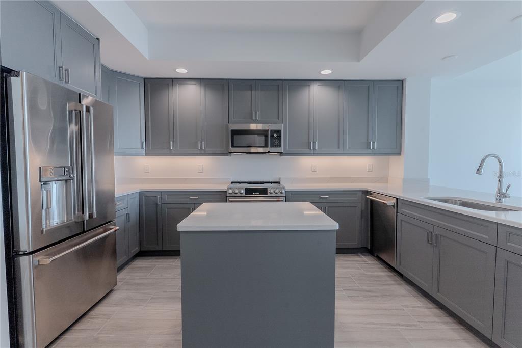 A modern kitchen features gray cabinets, stainless steel appliances, a center island, and white countertops — 125 ISLAND WAY UNIT 503, CLEARWATER BEACH, FL