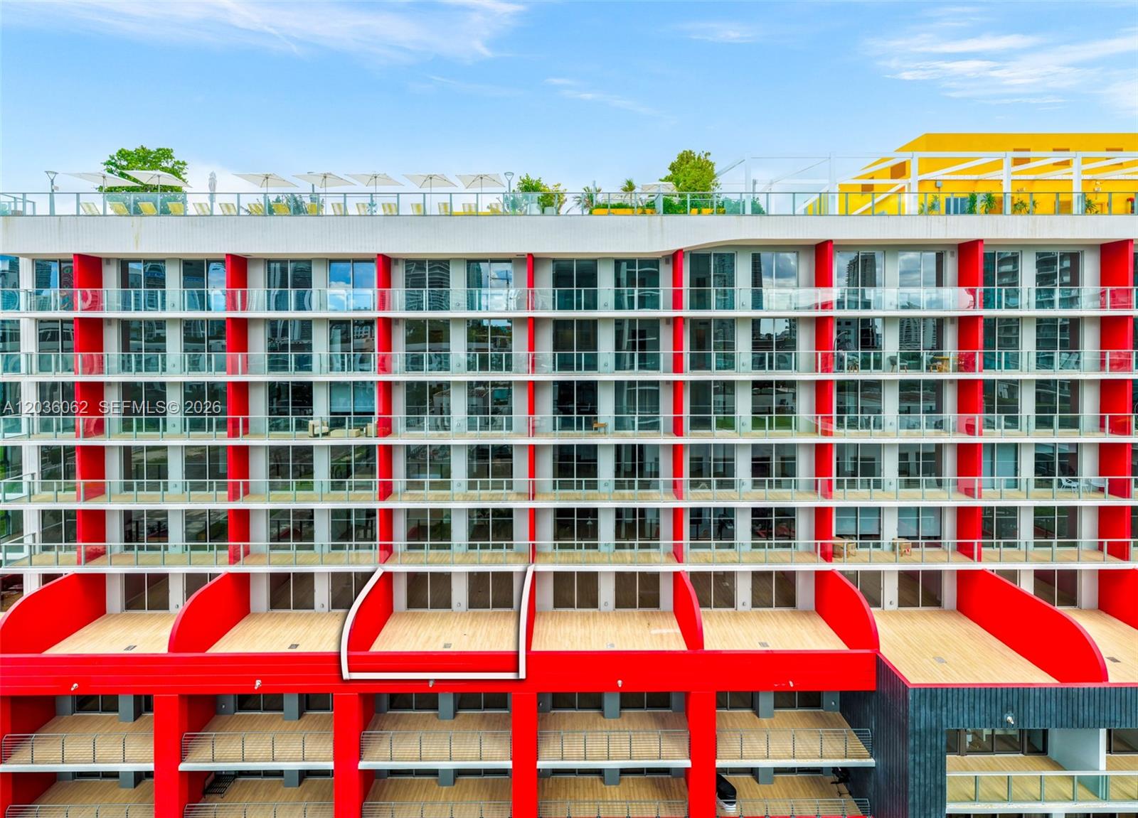 An exterior view of a modern apartment building featuring red structural accents and balconies — MIAMI, FL