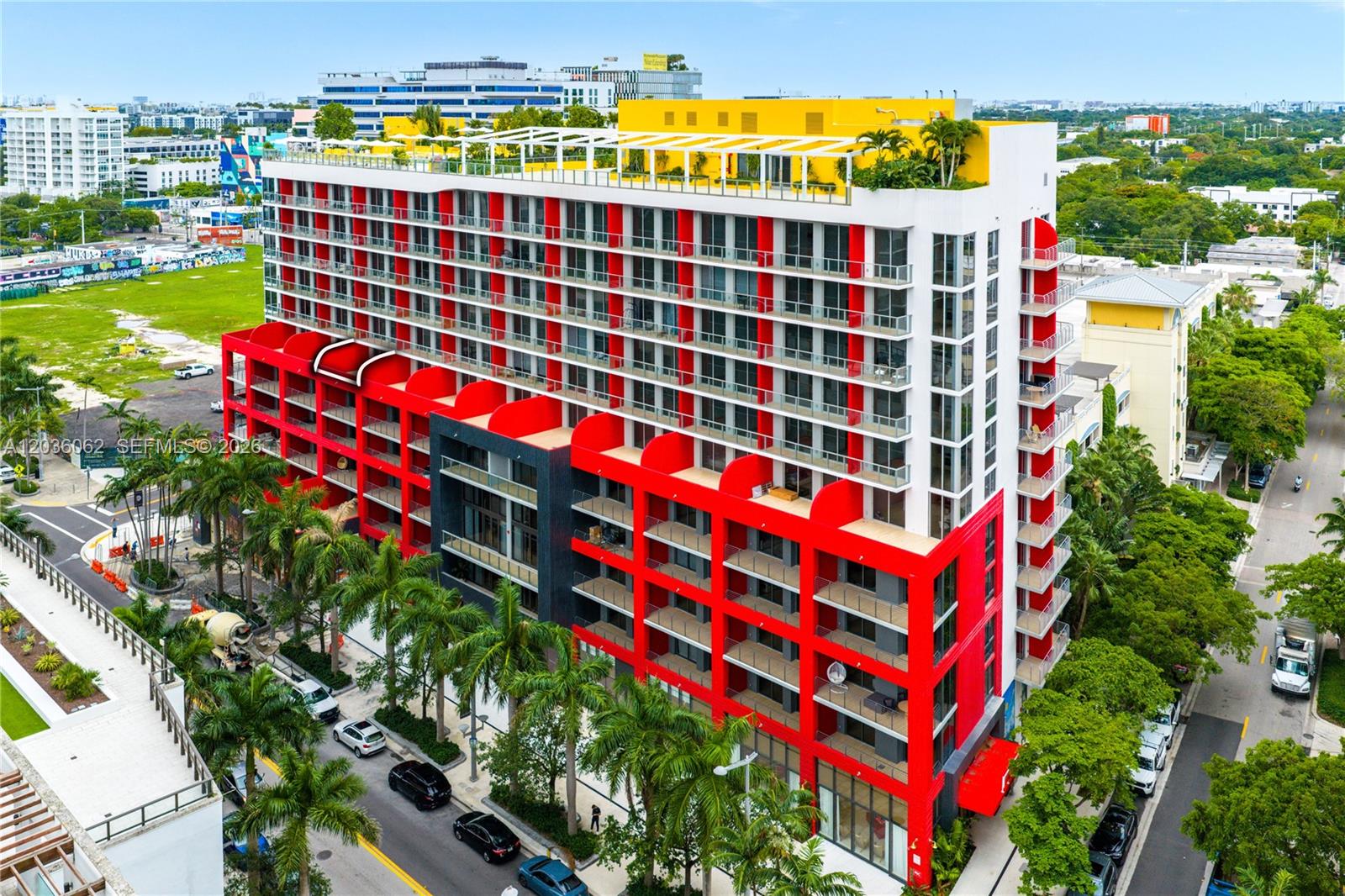 An aerial view of a modern apartment building featuring red accents and a rooftop terrace — MIAMI, FL