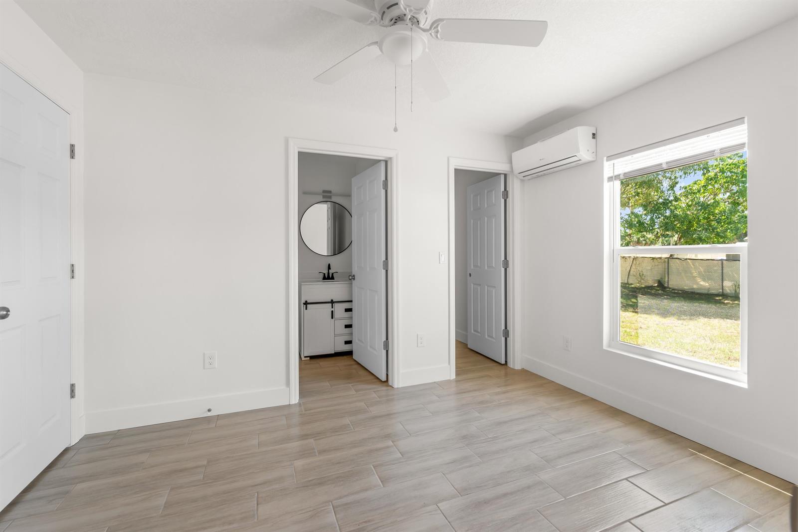 A bright bedroom features white walls, wood-look tile flooring, a ceiling fan, and an ensuite bathroom — 1135 17th Place, Vero Beach FL 32960, VERO BEACH, FL