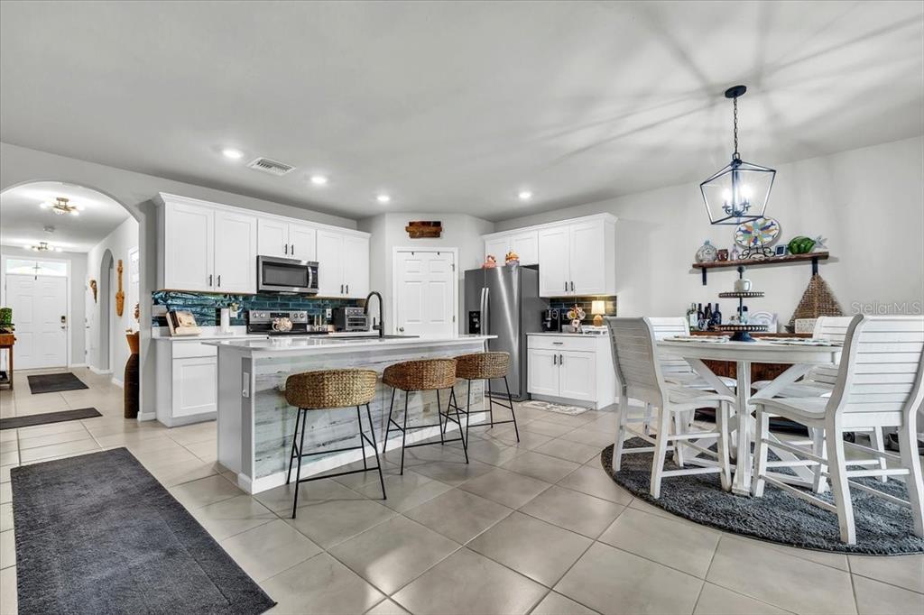 A kitchen features white cabinetry, a central island with bar stools, and a dining area — 25157 ALCAZAR, PUNTA GORDA, FL