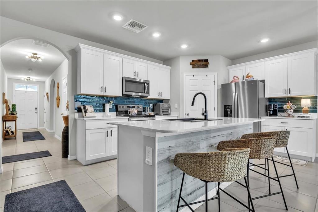 A kitchen features white cabinets, a blue tile backsplash, a kitchen island, and bar stools — 25157 ALCAZAR, PUNTA GORDA, FL