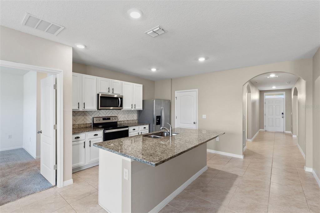 A kitchen with white cabinets, granite countertops, a center island, and tile flooring — 5725 SUNBONNET WAY, ST CLOUD, FL