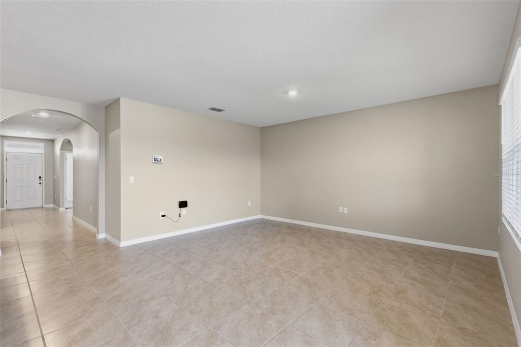 An empty living room features beige walls, light-colored tile flooring, and an arched entryway — 5725 SUNBONNET WAY, ST CLOUD, FL