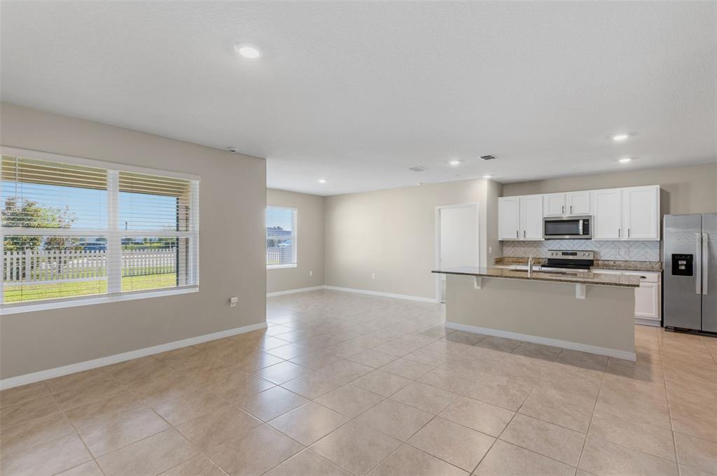An open-concept kitchen and living area features light tile flooring, white cabinets, and granite countertops — 5725 SUNBONNET WAY, ST CLOUD, FL