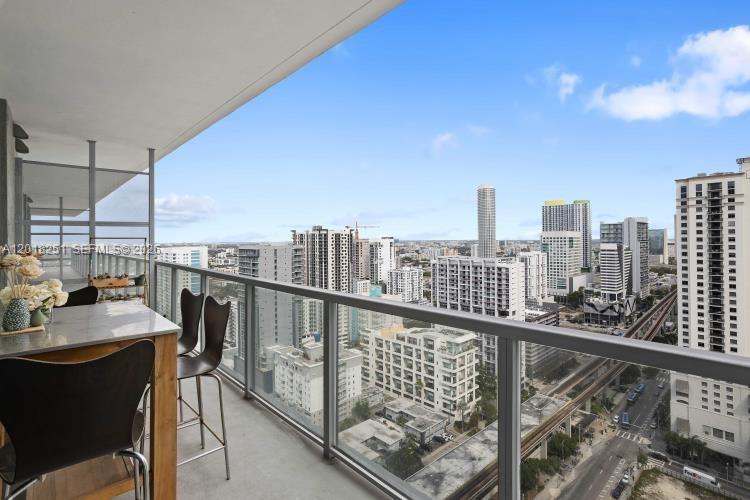A balcony with a high-top table and chairs overlooks a dense urban skyline — 79 SW 12th St, Miami FL 33130, MIAMI, FL