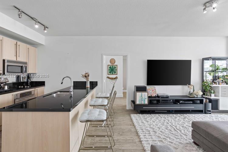 A modern kitchen with black countertops and light wood cabinets opens into a living area — 79 SW 12th St, Miami FL 33130, MIAMI, FL