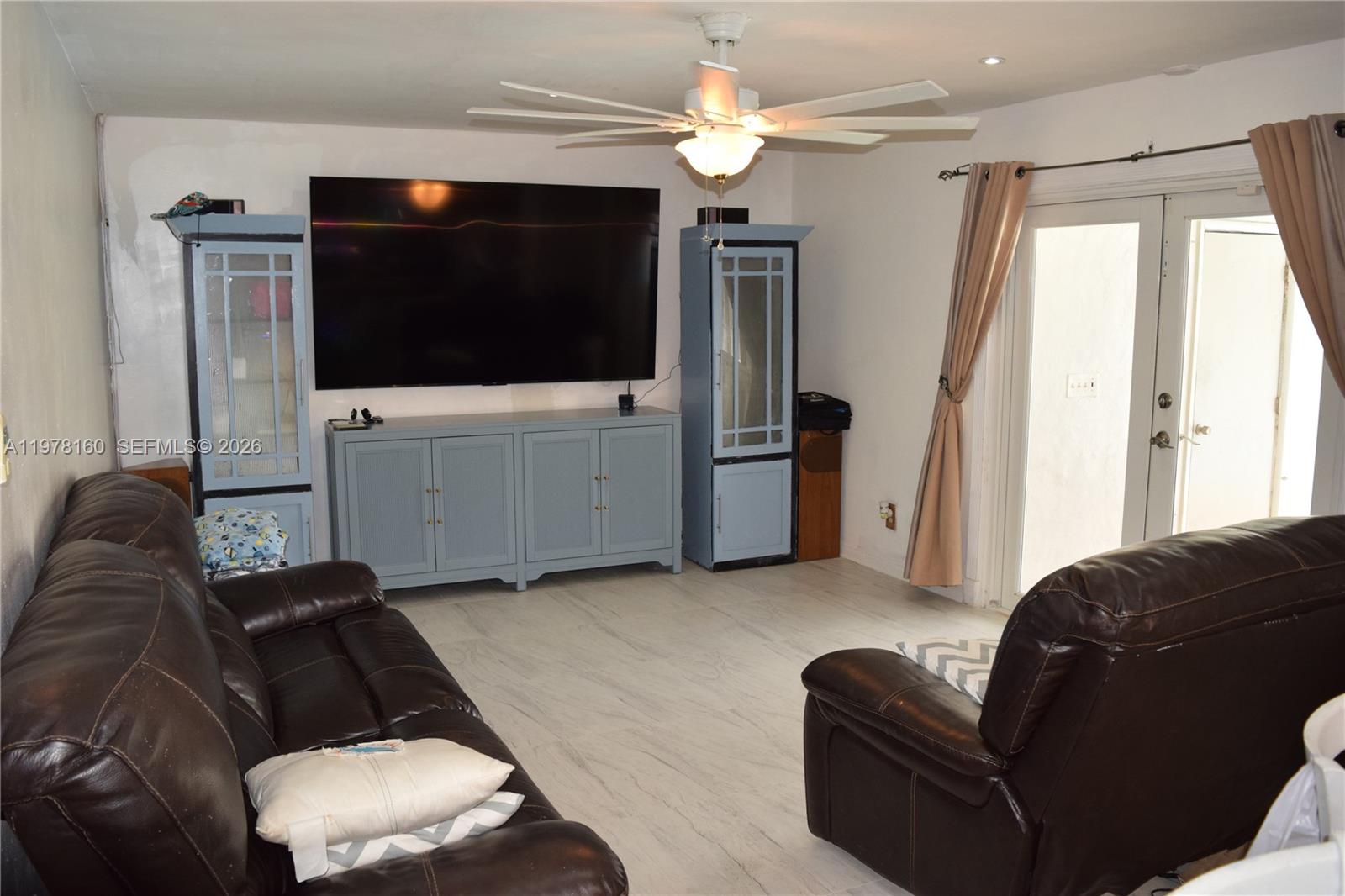 A living room features a large television, blue cabinetry, brown leather furniture, and tile flooring — 5317 Van Buren St, Hollywood FL 33021, HOLLYWOOD, FL