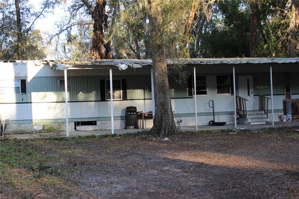 A single-story mobile home with a metal carport roof and a large tree in front — 5651 SE 33RD COURT, OCALA, FL