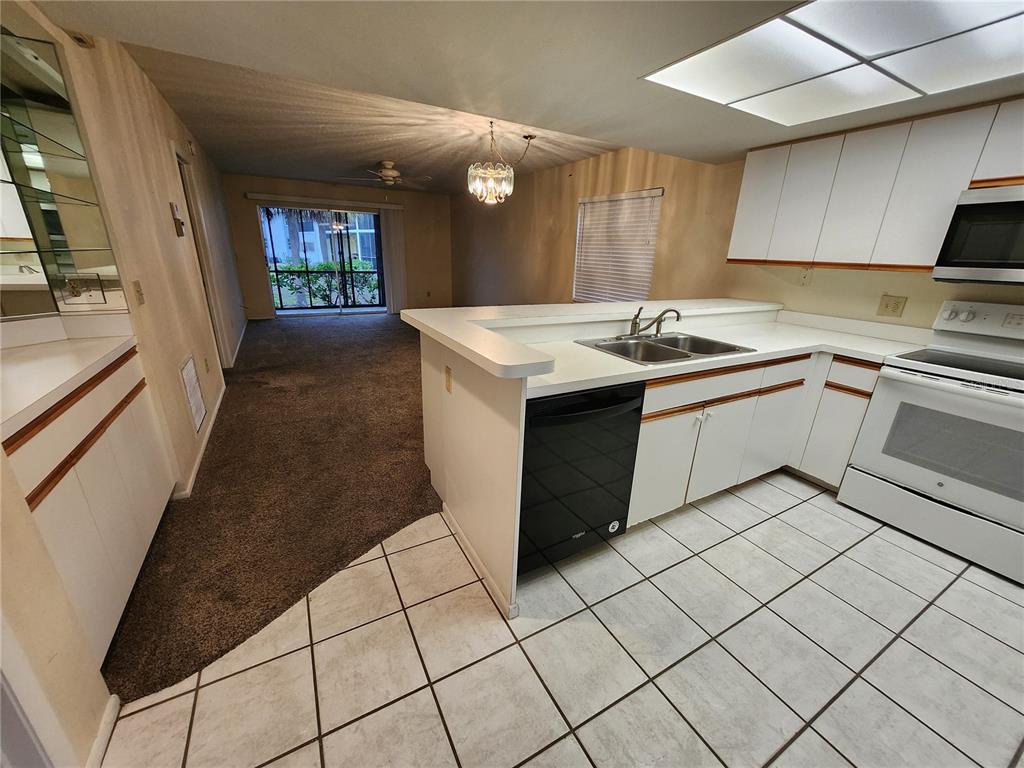 A kitchen with white cabinets, a black dishwasher, and tile flooring opens to a carpeted living area — 6800 PLACIDA ROAD UNIT 1004, ENGLEWOOD, FL