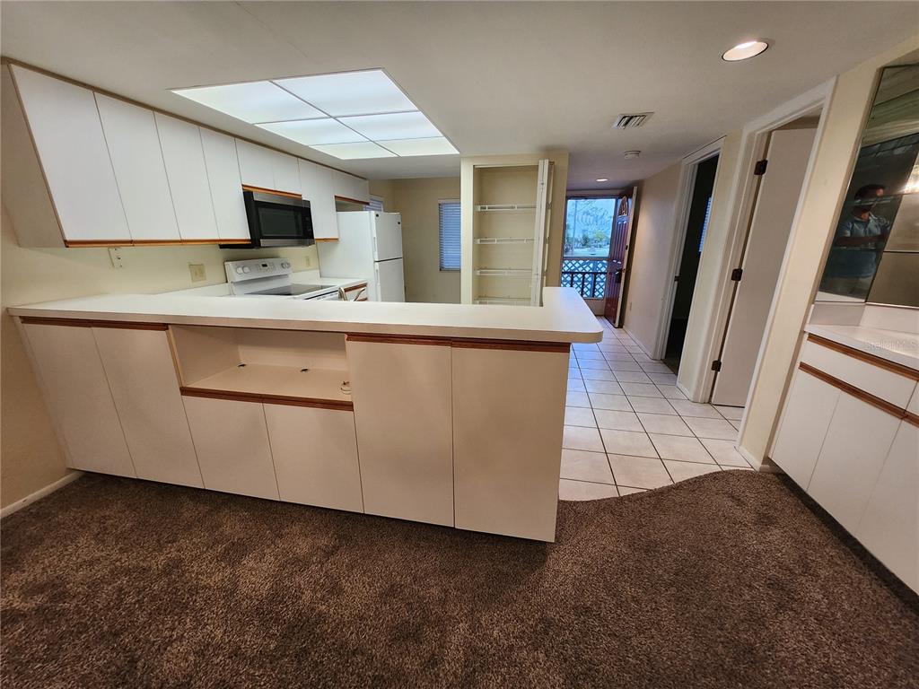 A kitchen with white cabinets, a breakfast bar, and carpeted flooring in the foreground — 6800 PLACIDA ROAD UNIT 1004, ENGLEWOOD, FL