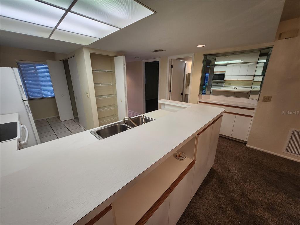 A kitchen with a white peninsula, double sink, pantry, and mirrored wall accents — 6800 PLACIDA ROAD UNIT 1004, ENGLEWOOD, FL