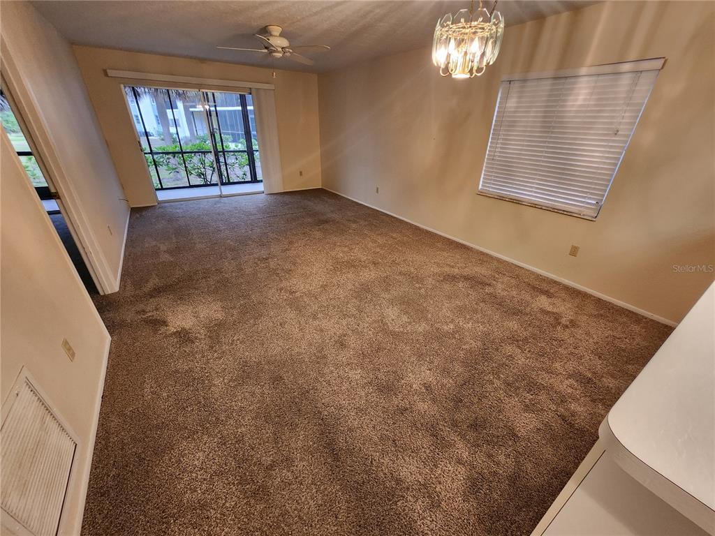An empty living room features brown carpet, a ceiling fan, and a sliding glass door — 6800 PLACIDA ROAD UNIT 1004, ENGLEWOOD, FL