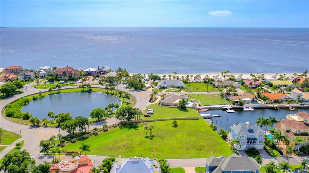 An aerial view shows a coastal neighborhood with a central pond, canal, and beach access — Lot 13 CAPTAINS COURT, NEW PORT RICHEY, FL