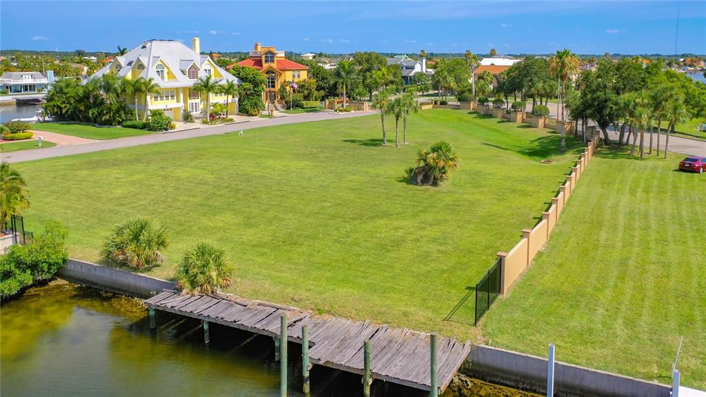 An aerial view shows a vacant, grassy waterfront lot with a wooden dock — Lot 13 CAPTAINS COURT, NEW PORT RICHEY, FL