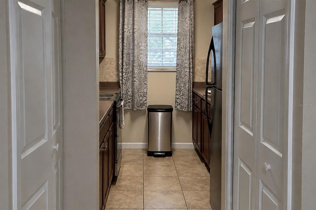 A galley-style kitchen features dark wood cabinets, stainless steel appliances, and a window with curtains — 4756 TANGERINE AVENUE UNIT 4756, WINTER PARK, FL